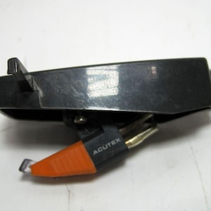 May include: A black and orange Acutex brand record player cartridge with a needle.