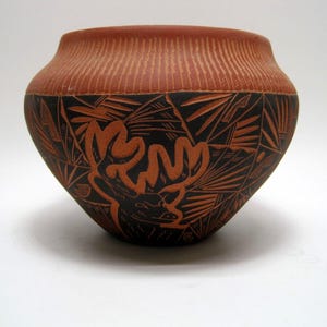 May include: A hand-crafted terracotta pottery bowl with a black and brown geometric design featuring a deer. The bowl has a textured surface and a rounded shape.
