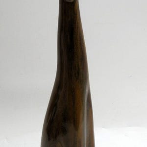 May include: A brown ceramic dog figurine with a long neck and slender body. The dog is sitting upright with its head held high, and its ears are perked up. The figurine has a glossy finish and is likely a decorative item.