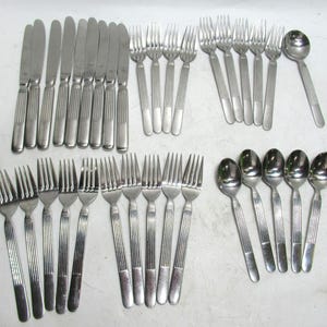 May include: A collection of stainless steel silverware, including knives, forks, and spoons. The silverware has a ridged handle design. The arrangement includes multiple sets of forks, knives, and spoons, suitable for a large gathering or dining setting.