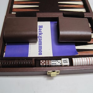 May include: A brown leather backgammon game set with a blue and white instruction booklet, dice, and checkers. The set is open and ready to play.