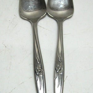 May include: Two silver serving utensils with floral designs on the handles. The utensils have a pointed tip and a small fork at the end.