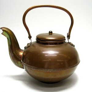 May include: A copper teapot with a rounded body and a curved handle. The teapot has a lid with a knob on top.