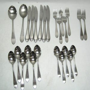 May include: A set of silverware, including spoons, forks, and knives, all made of stainless steel. The silverware is arranged in rows on a white surface.