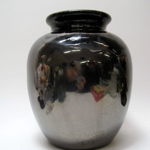 May include: A black ceramic vase with a shiny, metallic glaze. The vase has a rounded body and a slightly flared lip.