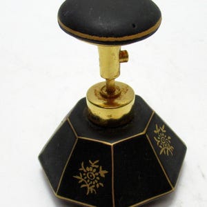 May include: A vintage perfume bottle with a black, faceted body and a gold-colored metal stem and top. The bottle features gold floral designs and a black, rounded stopper with a gold trim. The design is elegant and classic.