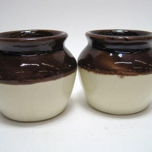 May include: Two brown and white ceramic crocks with a glazed finish.