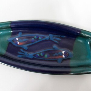 May include: Rectangular ceramic serving dish with a blue, teal, and purple color scheme. The dish features two stylized fish in blue with red and white accents. The edges are teal, and the center is a mix of blue and purple.