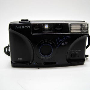 May include: A black Ansco Vision AF camera with a built-in flash. The camera has a lens with a 1:4.5 aperture and an auto focus feature.