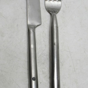 May include: A stainless steel knife and fork set. The knife has a straight blade and a rounded handle. The fork has four tines and a matching handle. The silverware is designed with a simple, modern aesthetic.