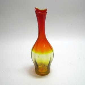 May include: A colorful glass vase with a slender neck and a flared base. The vase transitions from a vibrant red at the top to a warm orange in the middle, and finally to a yellow-green at the base. The vase has a unique, curved shape.