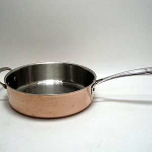 May include: A copper-bottomed stainless steel saucepan with a single handle. The handle is silver and has a curved design.
