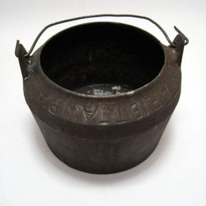 May include: A vintage cast iron pot with a wire handle. The pot has a dark brown patina and is marked with the words "The Favorite".
