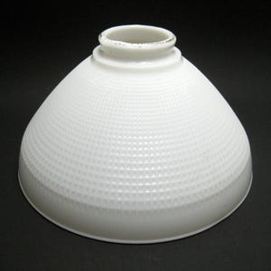 May include: A white, cone-shaped lampshade with a textured, geometric pattern. The lampshade has a rounded base and a small, cylindrical top. The surface is covered in a repeating pattern of small, raised triangles.