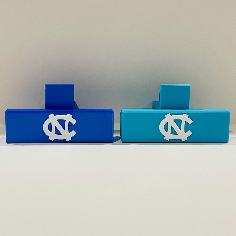 May include: Two rectangular, blue and teal-colored objects with a white "NC" logo. Each object has a smaller, square block on top. The objects are likely decorative or functional items.