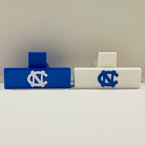 May include: Two rectangular, decorative objects, one blue and one white, each featuring a university logo. The blue object has a white logo, while the white object has a blue logo. Both have a small, square accent.