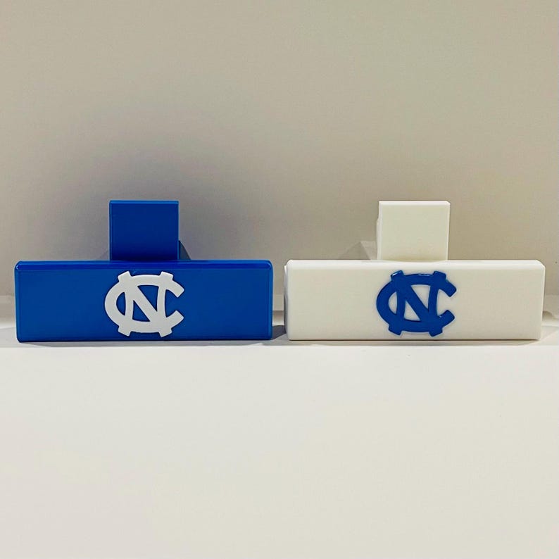 May include: Two rectangular, decorative objects, one blue and one white, each featuring a university logo. The blue object has a white logo, while the white object has a blue logo. Both have a small, square accent.