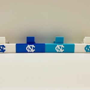 May include: A set of four white, blue, and teal decorative bars. Each bar features a white or blue logo with the letters "NC" in a stylized design. The bars are designed to stand upright and are likely used for display or decoration.