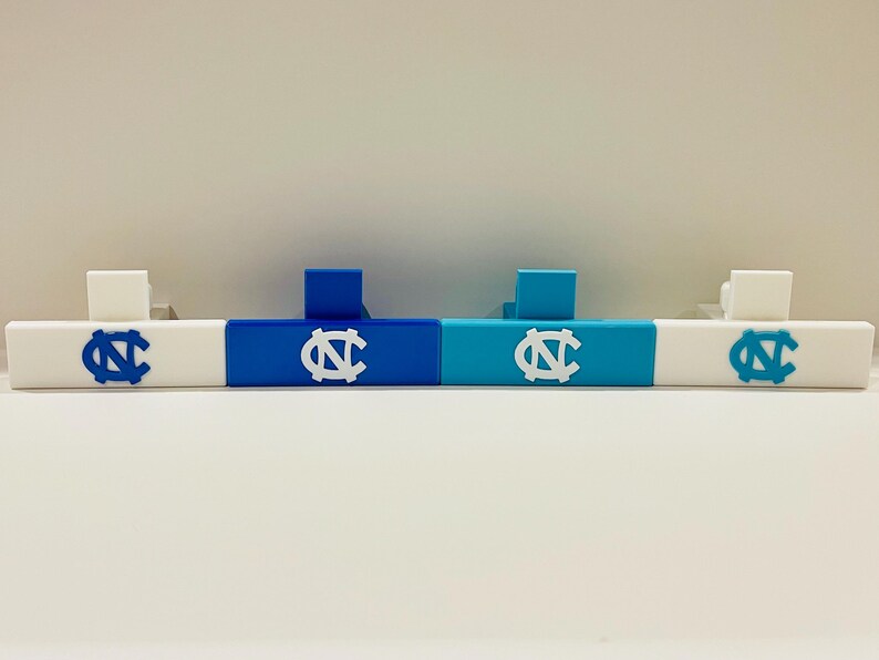 May include: A set of four white, blue, and teal decorative bars. Each bar features a white or blue logo with the letters "NC" in a stylized design. The bars are designed to stand upright and are likely used for display or decoration.