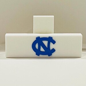May include: A white rectangular block with a smaller white square on top. A blue logo is centered on the front. The logo is a stylized letter "N" and "C" intertwined.