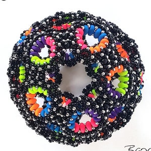 Puede incluir: Un orbe negro de cuentas con bucles de cuentas de colores arcoíris. El orbe es una forma de estrella 3D. El texto "Galaxy Star Orb" está escrito encima del orbe. El texto "The Beading Butterfly" está escrito debajo del orbe.