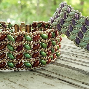 Puede incluir: Dos pulseras de cuentas con un patrón de chevron. La pulsera de la izquierda es verde, dorada y marrón. La pulsera de la derecha es morada, verde y plateada. Las pulseras están sobre una superficie de madera. El texto "The Beading Butterfly" es visible en el fondo.
