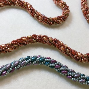 May include: Two beaded necklaces, one in shades of brown and gold, and the other in shades of blue, purple, and silver. The necklaces are twisted and have a rope-like appearance. The text "for The Beading Butterfly" is visible in the top right corner of the image.