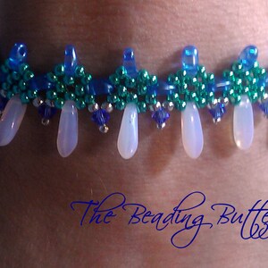 May include: A beaded bracelet with a blue, green, and silver color scheme. The bracelet has a fringe of white teardrop-shaped beads.