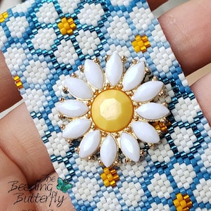 Peut inclure: Un bracelet en perles blanc et bleu avec un charme de marguerite jaune. Le bracelet a un motif à carreaux et la marguerite a un centre jaune.