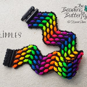 May include: A rainbow coloured beaded bracelet with black beads. The bracelet is made in a ripple pattern and has black clasps. The bracelet is labelled "RIPPLES" and "The Beading Butterfly".