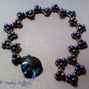 May include: A beaded bracelet with a dark blue and iridescent finish. The bracelet is made with small, round beads and features a repeating pattern of star shapes. A large, dark blue, faceted bead is attached to the bracelet.