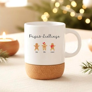 May include: A white ceramic mug with a cork base featuring the black text Papas Lieblinge and three gingerbread cookie illustrations labeled Oskar, Bella, and Leonard. The middle gingerbread figure wears a red bow, and the right figure wears a red scarf.