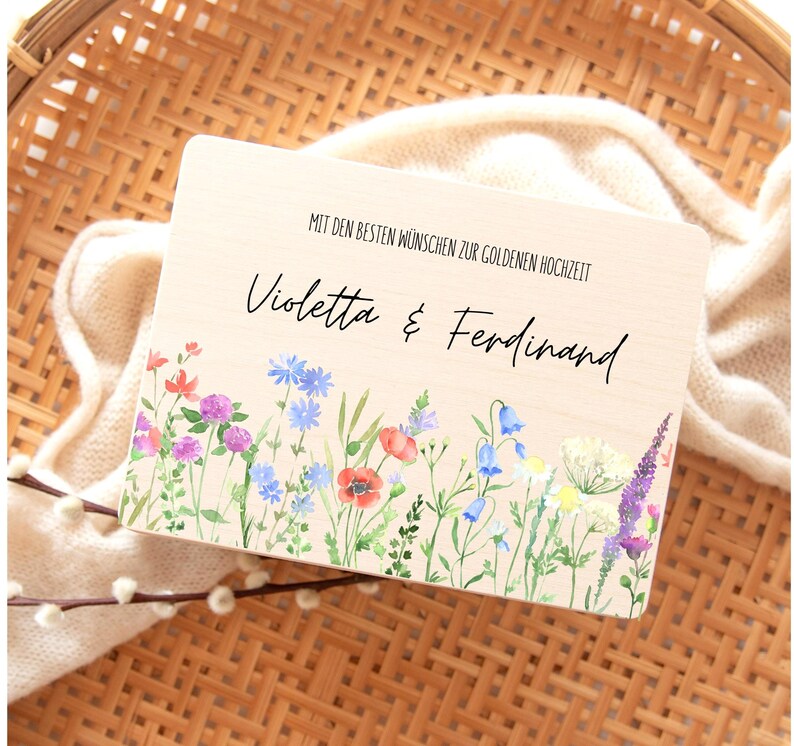 Puede incluir: Placa de madera con el texto "Violetta & Ferdinand" y "MIT DEN BESTEN W&Uuml;NSCHEN ZUR GOLDENEN HOCHZEIT". La placa presenta un borde floral de acuarela con amapolas rojas, campanillas azules y lavanda p&uacute;rpura. El fondo es de color beige claro.
