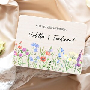Puede incluir: Una caja de madera con un dise&ntilde;o floral de acuarela con amapolas rojas, campanillas azules y lavanda p&uacute;rpura. La caja tiene los nombres "Violetta & Ferdinand" y el texto "MIT DEN BESTEN W&Uuml;NSCHEN ZUR ROSENHOCHZEIT".