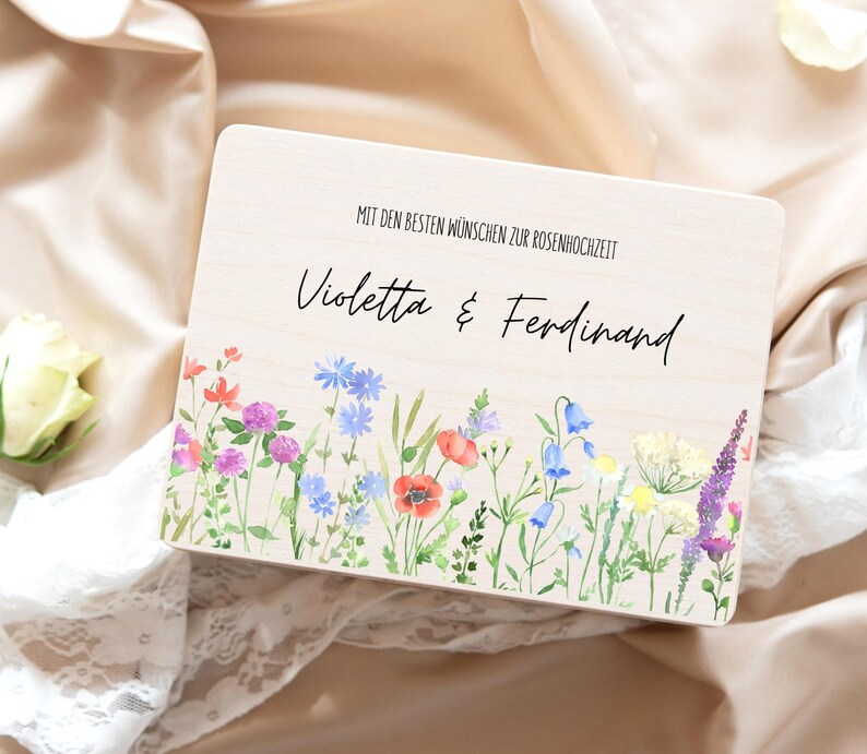 Puede incluir: Una caja de madera con un dise&ntilde;o floral de acuarela con amapolas rojas, campanillas azules y lavanda p&uacute;rpura. La caja tiene los nombres "Violetta & Ferdinand" y el texto "MIT DEN BESTEN W&Uuml;NSCHEN ZUR ROSENHOCHZEIT".