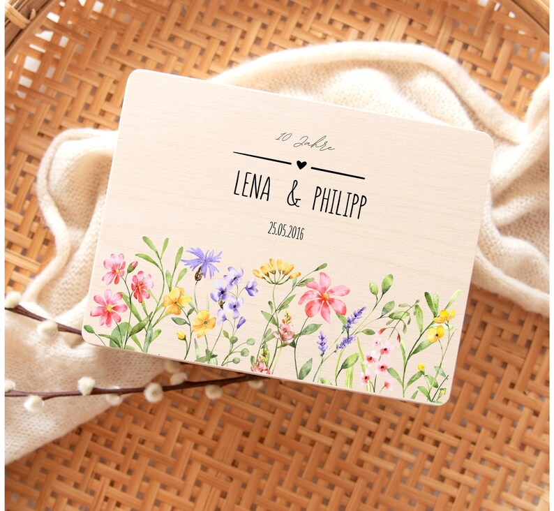 K&ouml;nnte beinhalten: Holzschild mit den Namen "LENA & PHILIPP" und dem Datum "25.05.2016" in Schwarz. Es hat einen floralen Rand mit rosa, gelben und lila Blumen. Der Text "10 Jahre" steht &uuml;ber den Namen.