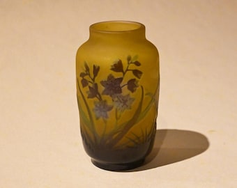 May include: A small, yellow-brown glass vase with a floral design. The vase has a dark brown base and features a pattern of blue and purple flowers with green leaves.