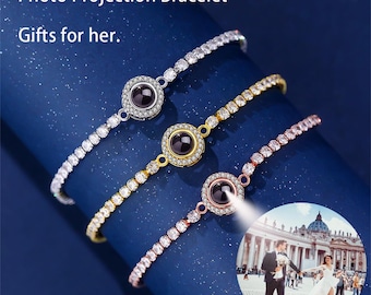 Op de afbeelding: Drie fotoprojectiearmbanden in zilver, goud en roségoud. Elke armband heeft een centrale cirkelvormige bedel met een geprojecteerde afbeelding, omringd door sprankelende stenen. De armbanden worden weergegeven op een donkerblauwe achtergrond. Tekst luidt "Photo Projection Bracelet" en "Gifts for her."