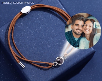 May include: A brown leather bracelet with a silver clasp and a small black stone that projects a photo when held up to a light source. The text "LOVE AT FIRST SIGHT" and "PROJECT CUSTOM PHOTOS" is visible above the bracelet.