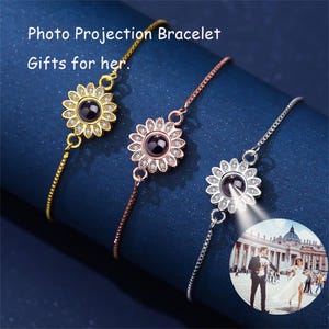 Puede incluir: Tres pulseras plateadas con un diseño de girasol. Cada pulsera tiene una pequeña piedra redonda negra en el centro del girasol. Las pulseras están sobre un fondo azul. El texto "Photo Projection Bracelet Gifts for her" está en la parte superior de la imagen.