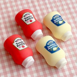 May include: Four novelty squeeze bottles, two red and two yellow, resembling ketchup and mayonnaise. The red bottles have a label that reads "Kawaii Tomato Ketchup". The yellow bottles have a label that reads "Kawaii Delicious Mayonnaise". Each bottle is approximately 400g.