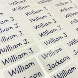 May include: A sheet of white rectangular labels with rounded corners, printed with the name "William" and "William J." in a dark blue, handwritten-style font. Some labels also include the name "Jackson".