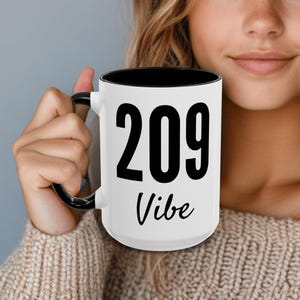 May include: White ceramic mug with a black interior and handle. The mug has black text that reads "209 Vibe".