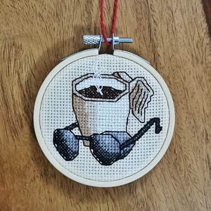 Peut inclure: Un cerceau de broderie blanc avec un motif de point de croix représentant une tasse de café avec une tasse de café fumante et des lunettes de soleil.