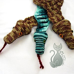 May include: A crocheted snake scarf with three heads. The heads are brown and green with orange eyes. The scarf is made with a variety of stitches and colors.
