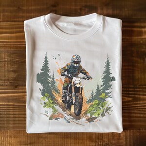 May include: White t-shirt featuring a graphic print of a person riding a dirt bike through a forest. The design incorporates a splash of colour and a green and brown colour scheme.