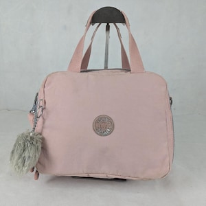 Peut inclure: Un sac à main rose clair avec une poignée supérieure et une bandoulière amovible. Le sac a un logo rond sur le devant et un porte-clés gris duveteux. Le sac est fait d'un matériau léger et durable.