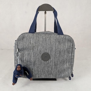 May include: A gray travel bag with a textured pattern, featuring navy blue handles and a matching monkey keychain. The bag has a circular logo on the front and navy blue zipper pulls.