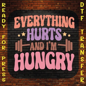 May include: A black brick wall with a yellow sign that says "READY FOR PRESS" on the left and "DTF TRANSFER" on the right. The sign has a black background with white text. The sign also has a pink, orange, and purple graphic that says "EVERYTHING HURTS AND I'M HUNGRY" with a barbell on either side of the text.