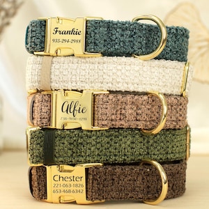 Peut inclure: Une pile de cinq colliers pour chiens de différentes couleurs : vert d'eau, crème, marron, vert olive et marron foncé. Chaque collier est doté d'une boucle dorée gravée d'un nom et d'un numéro de téléphone. Les colliers sont en tissu texturé.